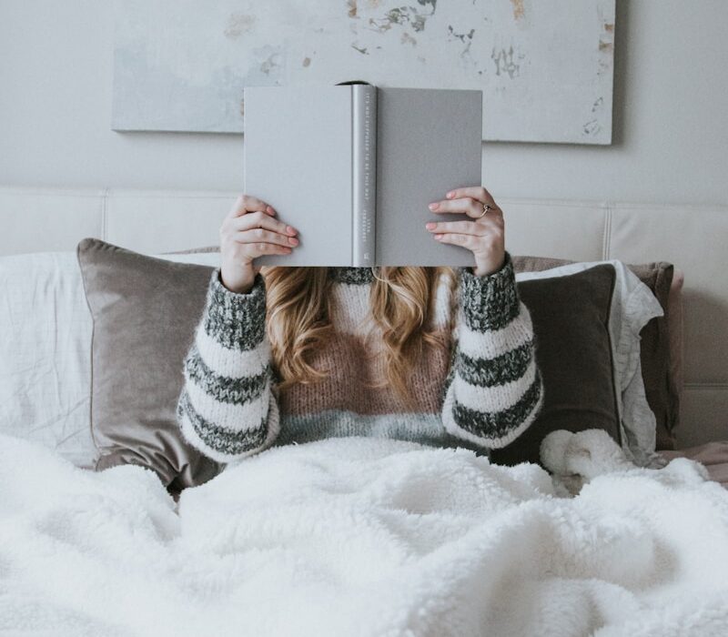 woman sitting on bed while holding book