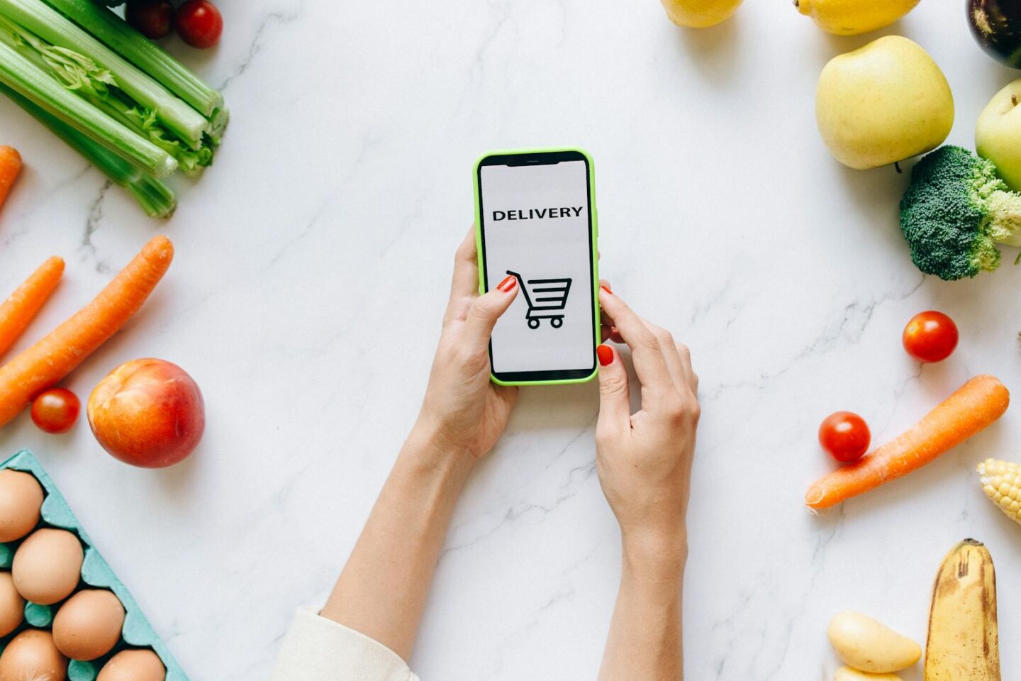 Person Holding a Mobile Phone with Scattered Fruits and Vegetables