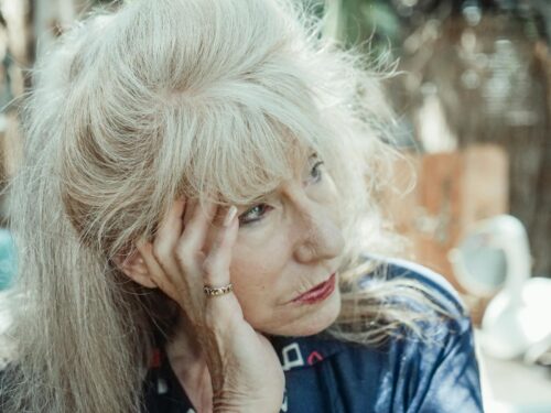 An introspective senior woman in thought, sitting outdoors on a sunny day.