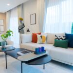 A modern living room with a white sofa and curtains, colorful throw pillows, and a decorative mannequin.