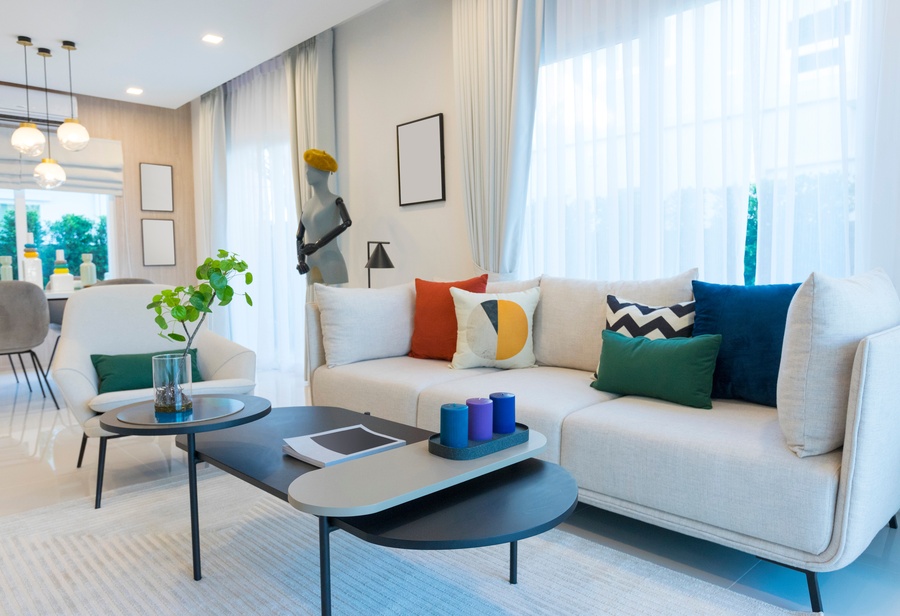 A modern living room with a white sofa and curtains, colorful throw pillows, and a decorative mannequin.