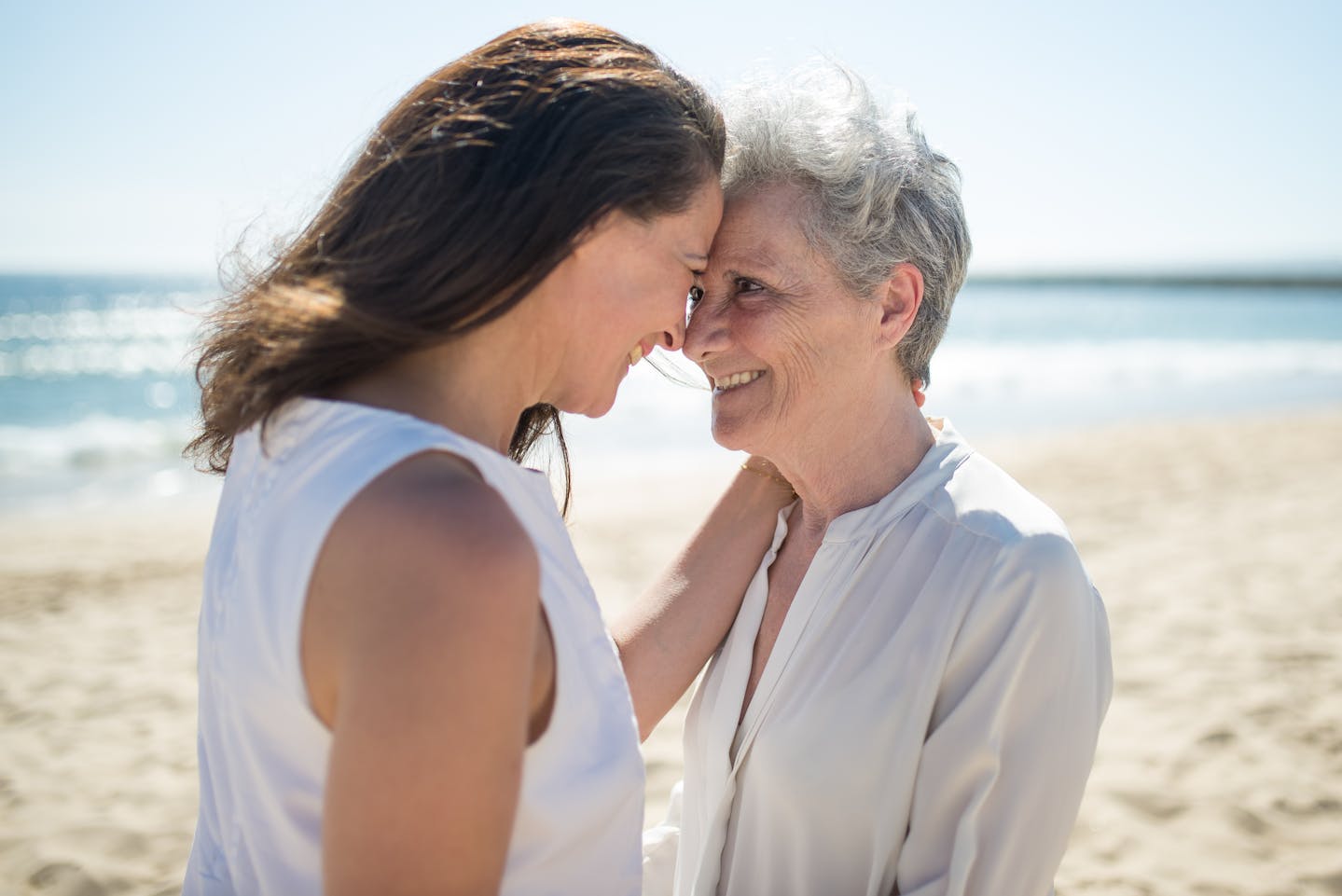 A mother and daughter share a tender moment on a sunny beach day, expressing joy and togetherness.